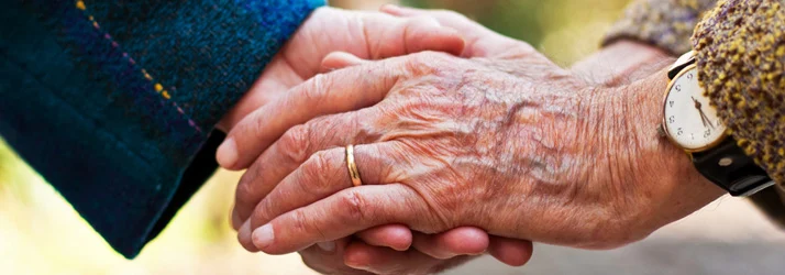 Close-up of two hands gently holding each other, symbolizing care, support, and connection, with one person wearing a wristwatch.